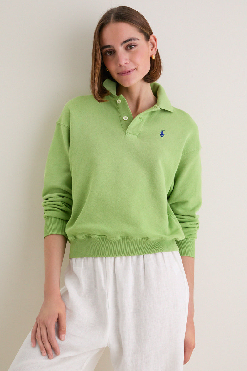 Young woman models a Parakeet Green Island Fleece Knit Polo, showcasing its classic, effortless style with relaxed fit and iconic embroidered logo, paired with white linen trousers.