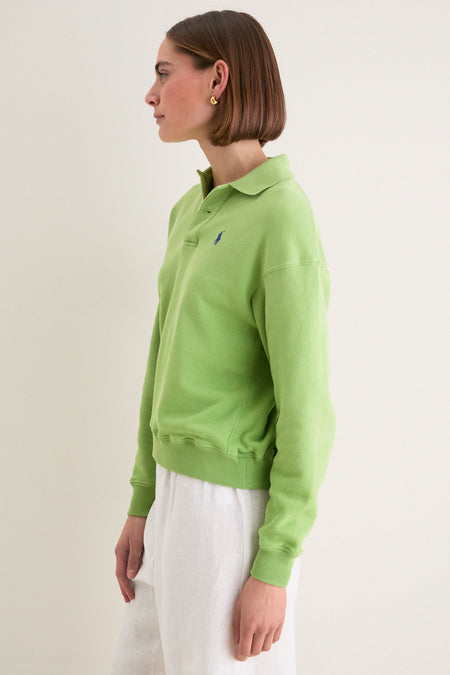 Person in profile wearing Parakeet Green Island Fleece Knit Polo and white trousers, showcasing classic, effortless style with relaxed fit and iconic embroidered Pony detail.