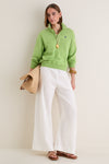 Model in Parakeet Green Island Fleece Knit Polo with a popped collar, paired with white linen trousers and a straw tote, exuding effortless, classic style.