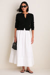 Model wearing Gloss Black Lyna Sunglasses, paired with a classic black cardigan and white skirt, exuding an effortless, high-end style with fun, bold eyewear.