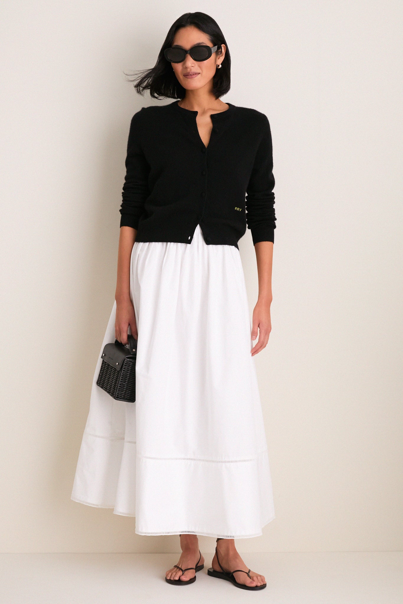 Model wearing Gloss Black Lyna Sunglasses, paired with a classic black cardigan and white skirt, exuding an effortless, high-end style with fun, bold eyewear.