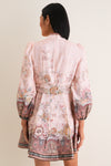 Woman in a classic, floral-print Pink Paisley Alchemy Button Mini Dress with puffed sleeves, featuring a scarf belt and jewel buttons, exuding effortless high-end style.