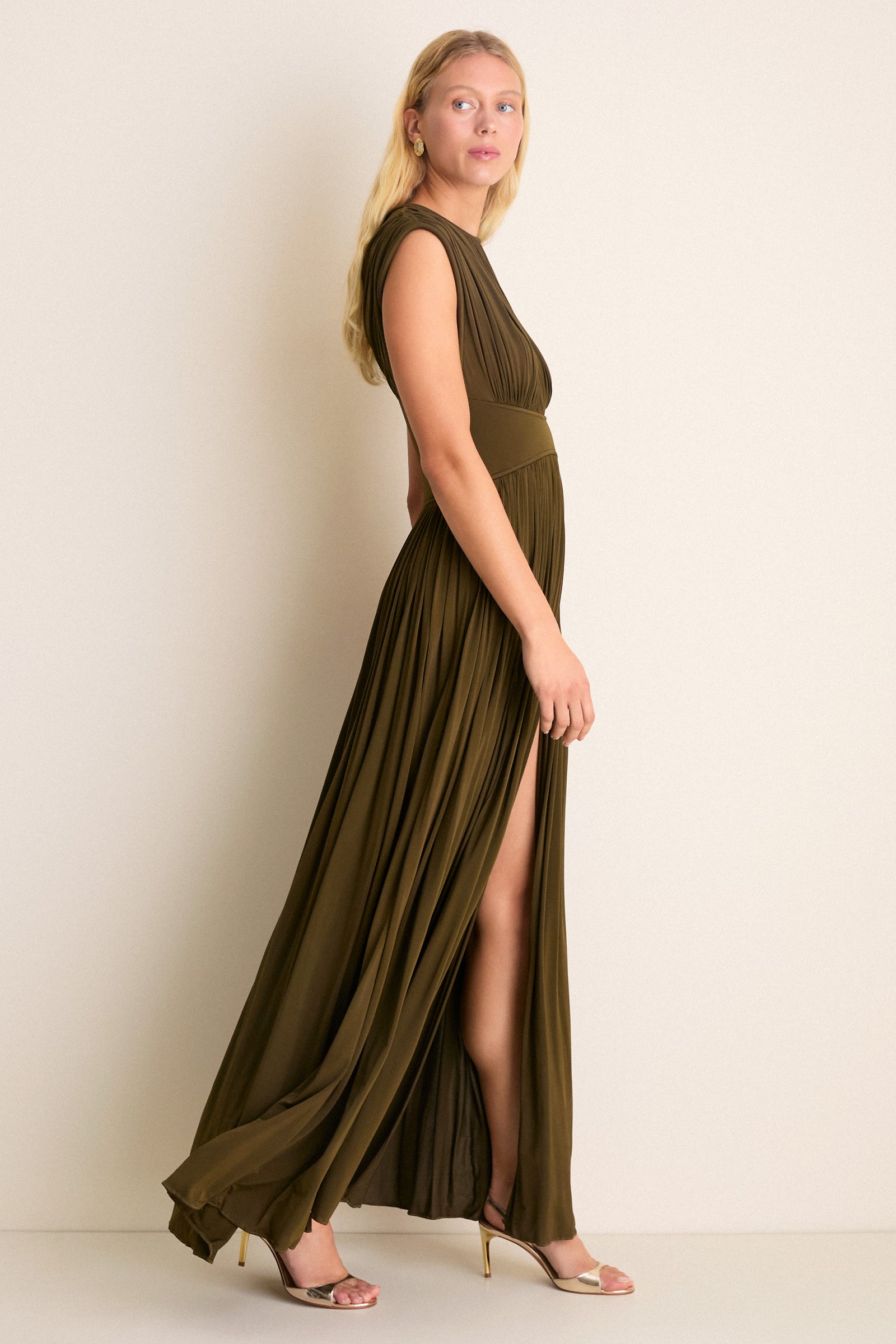 Olive Luna Column Dress: A classic, sleeveless gown with a fixed waistband, front skirt splits, and pleated fabric, paired effortlessly with metallic gold heels for high-end elegance.