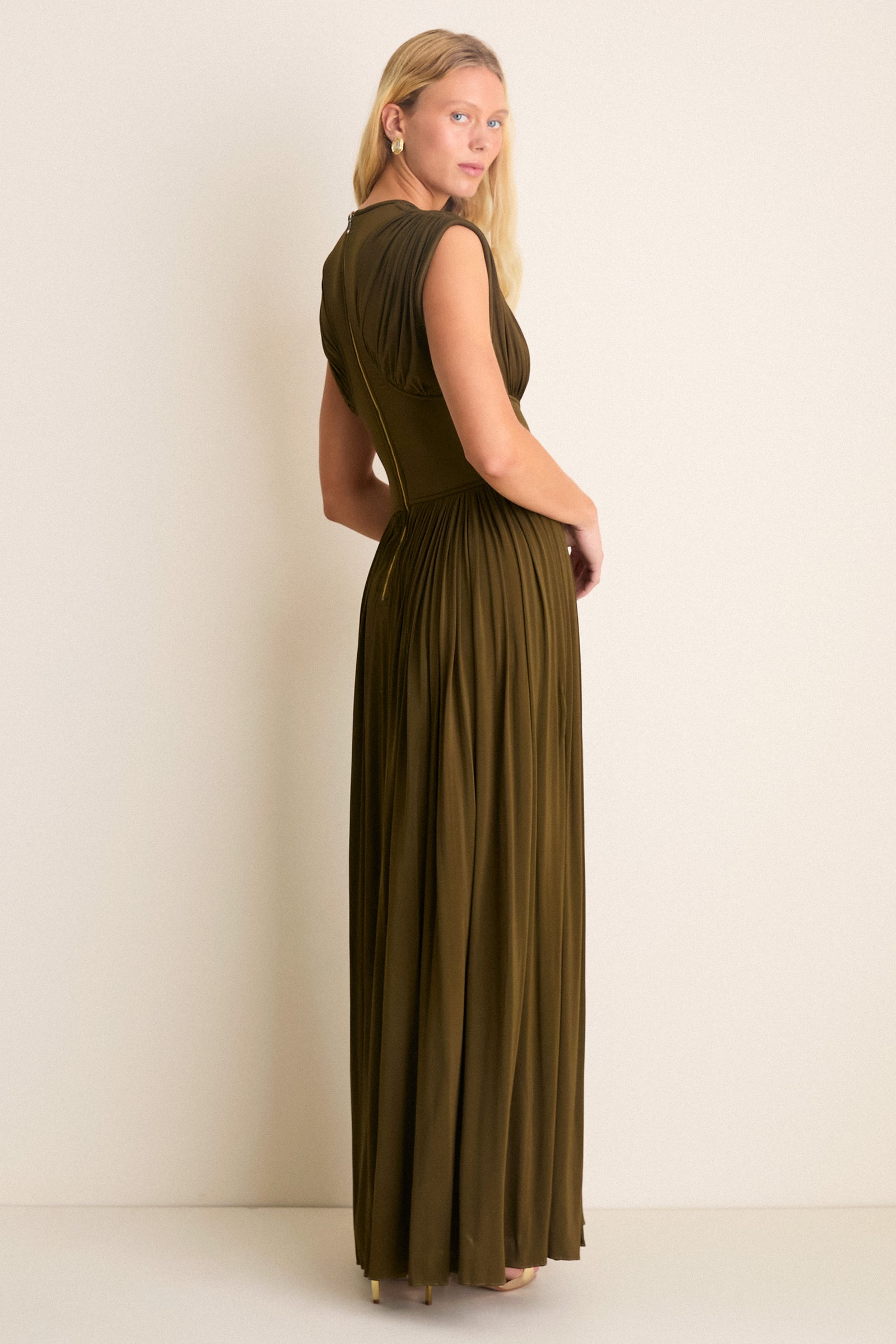 Woman in Olive Luna Column Dress with pleated skirt, front splits, and gold zip, exuding classic, effortless style. Perfect for high-end occasions, embodying fun sophistication.