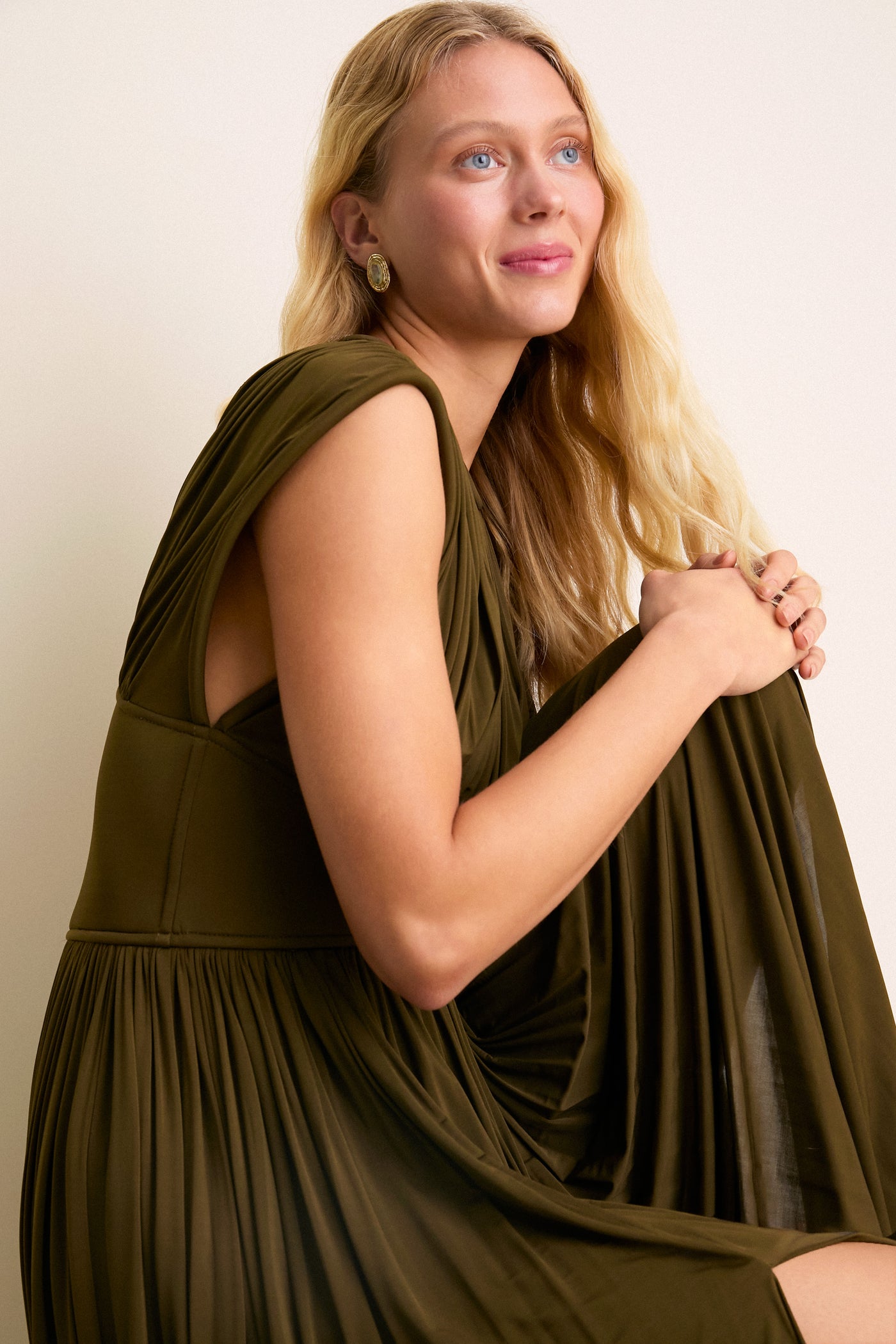 Effortlessly classic, the Olive Luna Column Dress features a pleated design and front splits, worn with gold earrings, embodying a fun, high-end elegance.