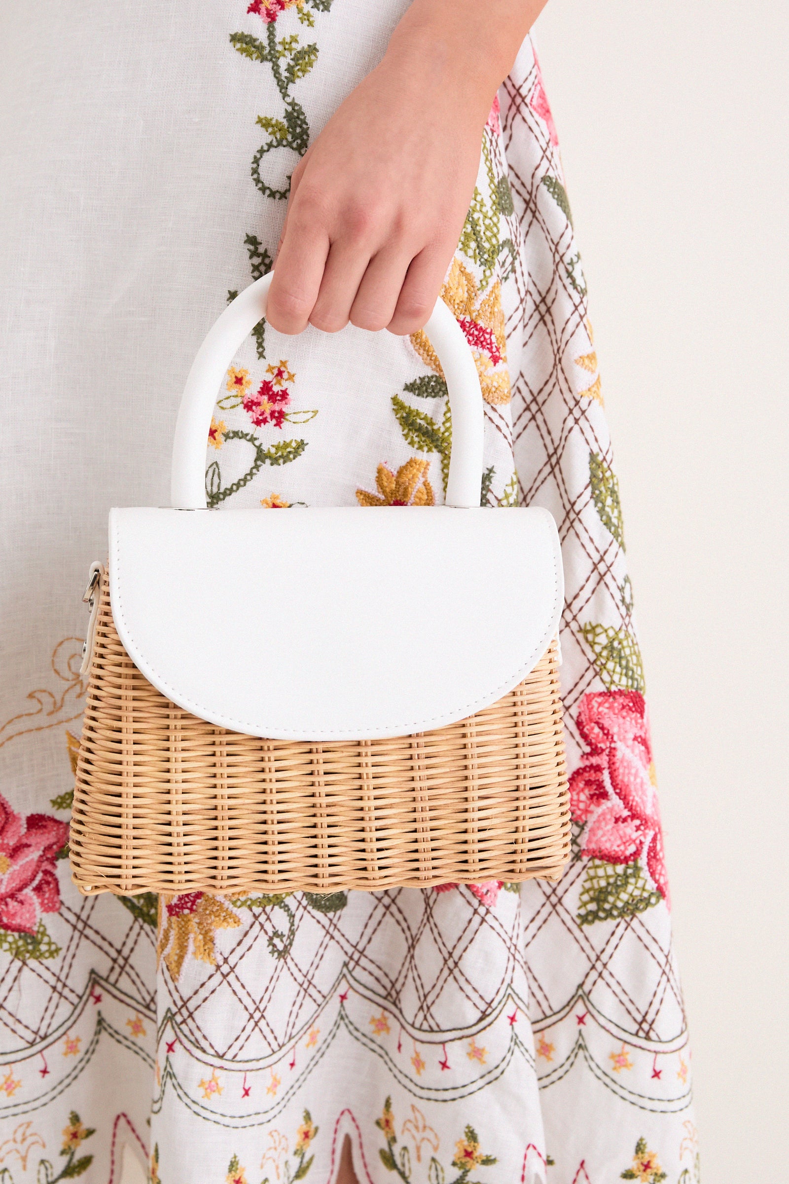 White Elle Wicker Top Handle bag, featuring a classic wicker body and sleek vegan leather trim, effortlessly held by a hand, exuding high-end and fun summer style.