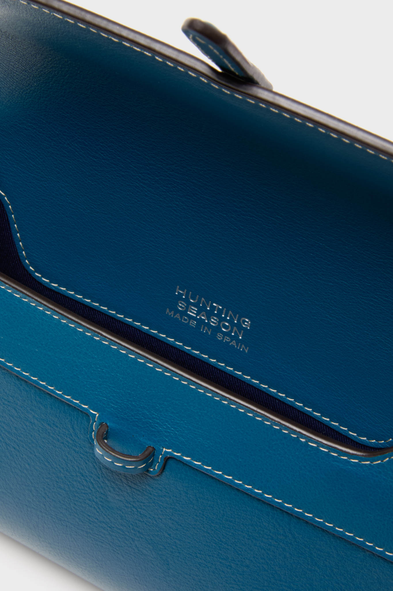 Teal Small Soft Clutch with white topstitching and gold-foil HUNTING SEASON – MADE IN SPAIN stamp, showcasing its classic, effortless, and high-end craftsmanship.