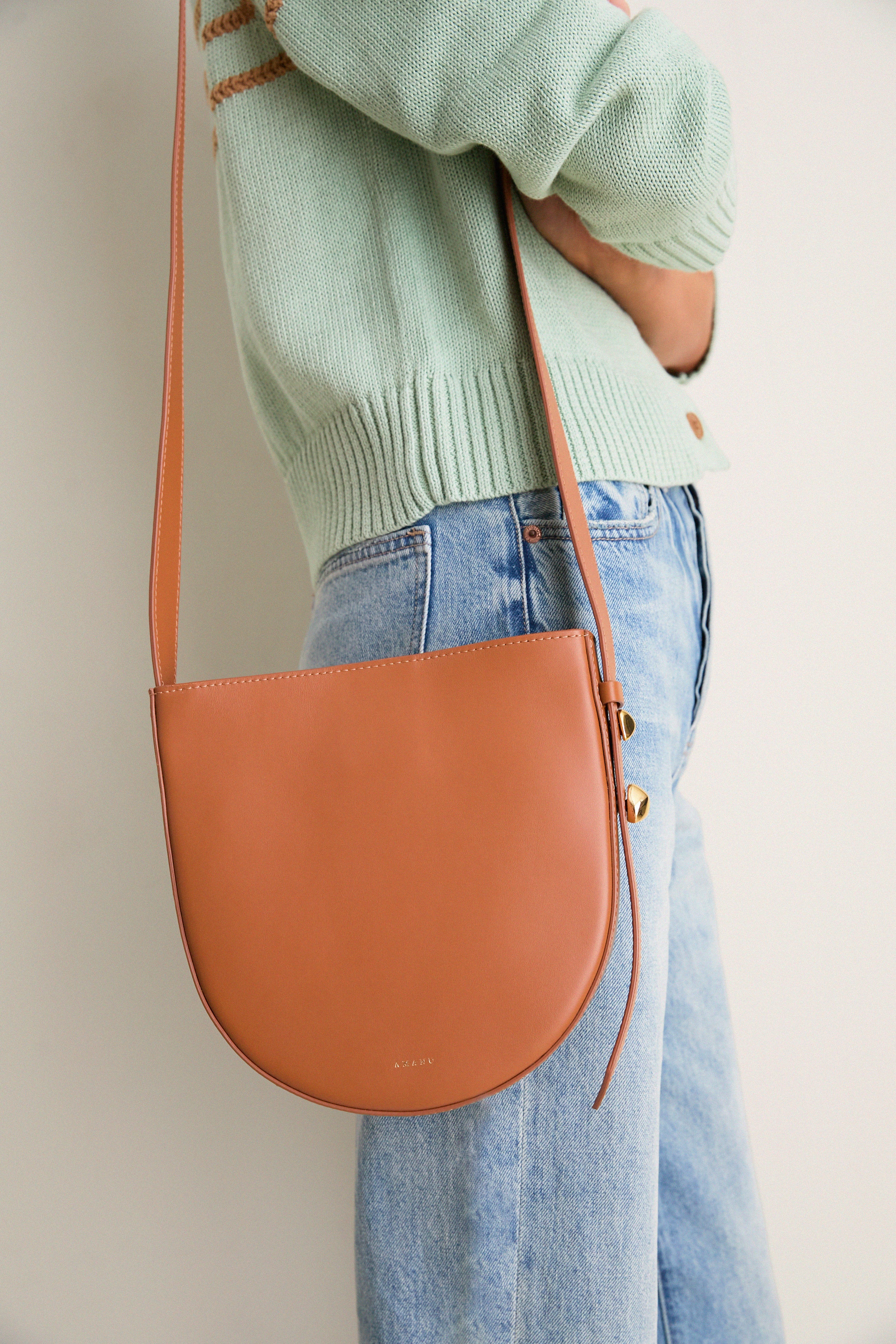 Cognac Leather Nigeria Crossbody: a classic, high-end leather bag with a minimal, effortless design, featuring a thin strap and sculptural gold-tone hardware for a fun, versatile look.