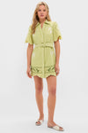 Woman models the classic Pastel Mint Poppy Mini Dress with scalloped hems, embroidered motifs, and a removable belt, styled effortlessly with off-white sandals for a fun, high-end look.