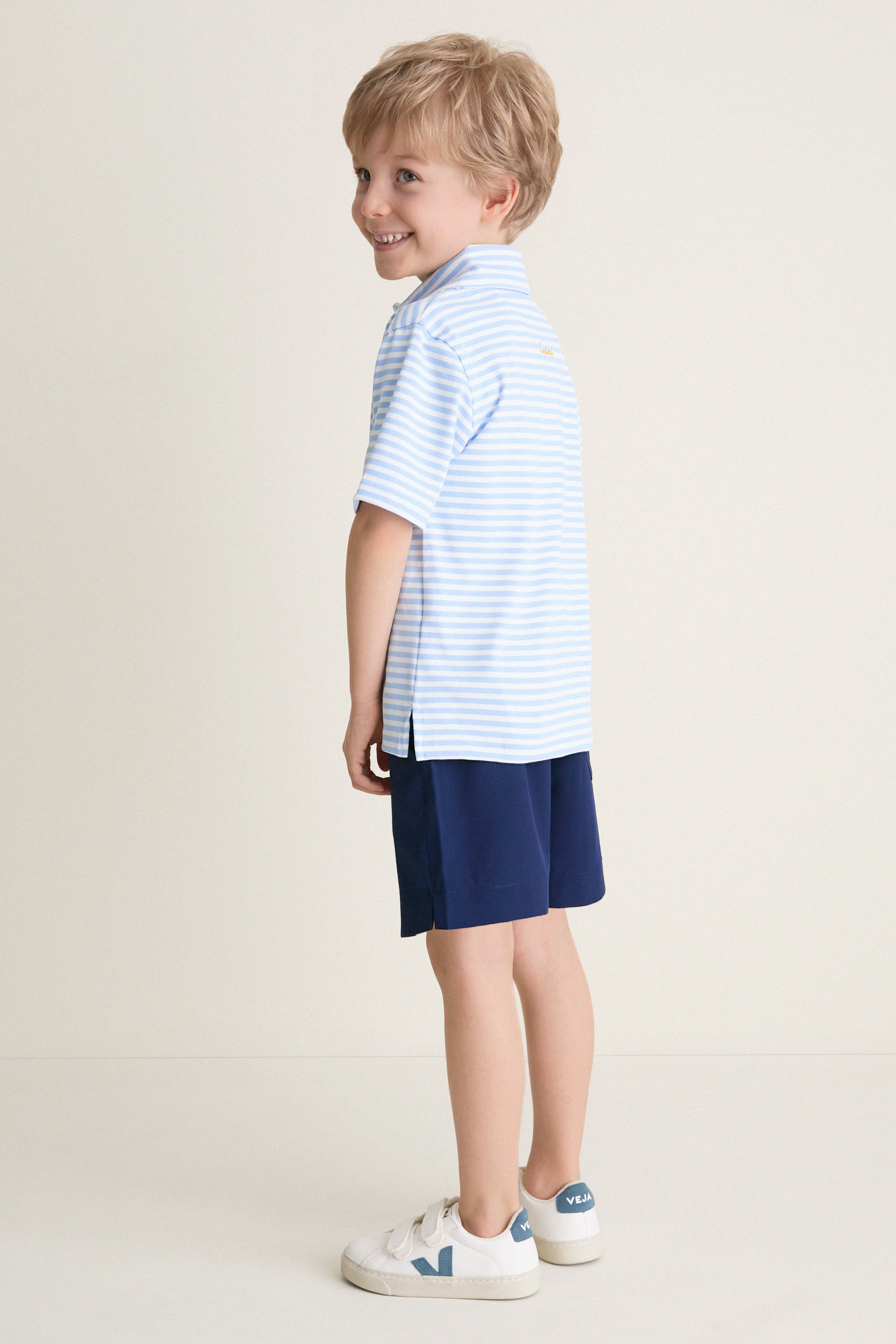 Young boy in profile wearing Nautical Navy Le Club Short and striped polo, embodying classic, effortless style with high-end, fun appeal. Perfect for polished, everyday wear.