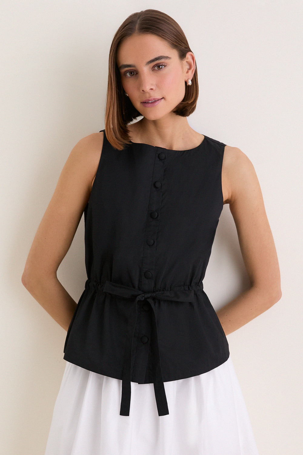 Young woman wearing a classic, high-end Black Cotton Poplin Francoise Top with a high neckline, sleeveless design, and cinched waist, embodying effortless sophistication and fun style.