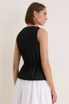 Woman in a sleeveless, classic Black Cotton Poplin Francoise Top with high neckline and cinched waist, exuding effortless sophistication against a simple backdrop.
