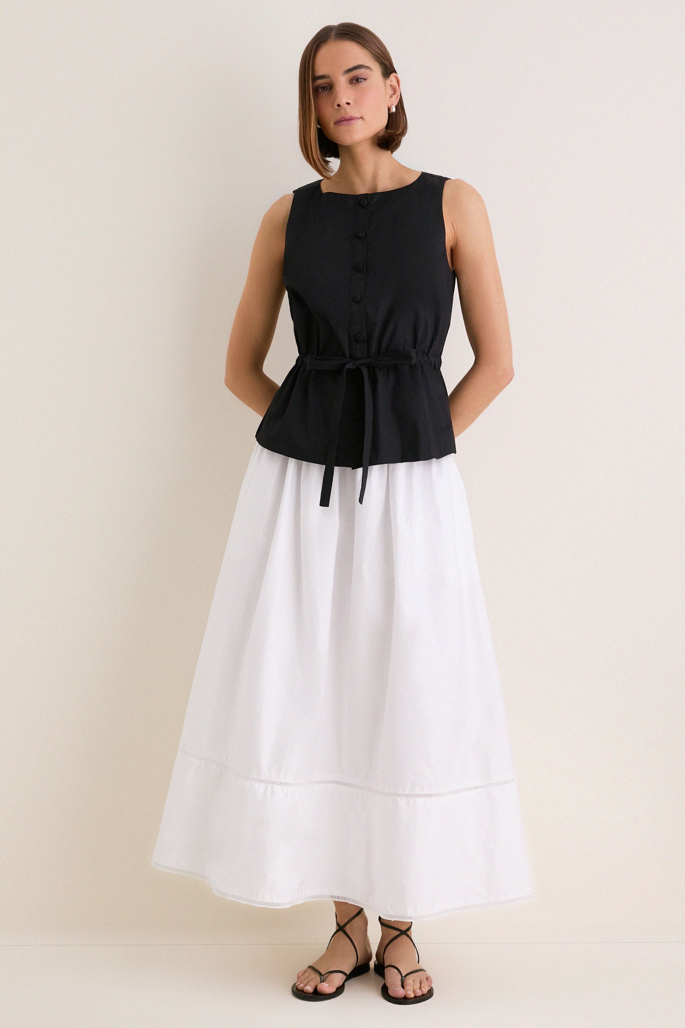 Woman models the Black Cotton Poplin Francoise Top, showcasing its classic high neckline and effortless cinched waist, paired with a flowing skirt for a high-end, fun look.