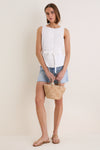 Young woman wears the classic White Cotton Poplin Francoise Top with high neckline and cinched waist, paired with frayed denim shorts and gold sandals, exuding effortless, high-end style.