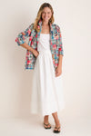 Woman standing in front of a white backdrop in a white tank and skirt and a madras blazer. 