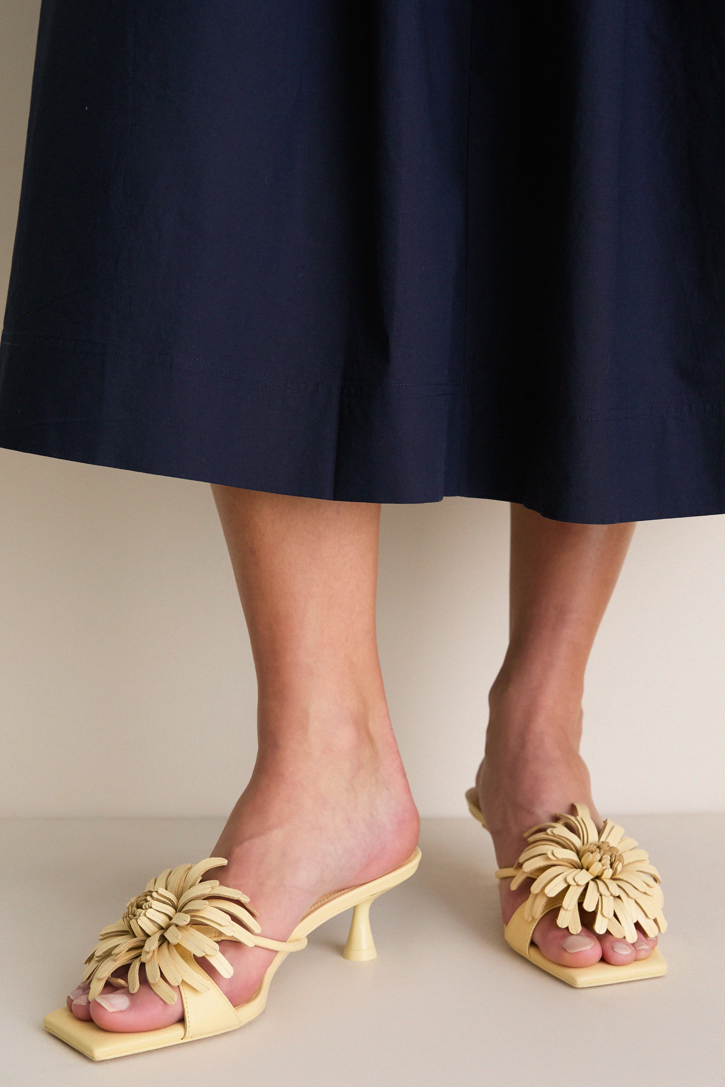 Buttercream Alora Low Heel: Effortlessly chic mule sandals with a classic square toe, playful floral embellishment, and a sculptural heel, perfect for high-end, fun fashion.