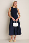 Woman in navy smocked midi dress, holding a white handbag, wears Buttercream Alora Low Heel—classic mule with floral appliqués for an effortless, high-end look.