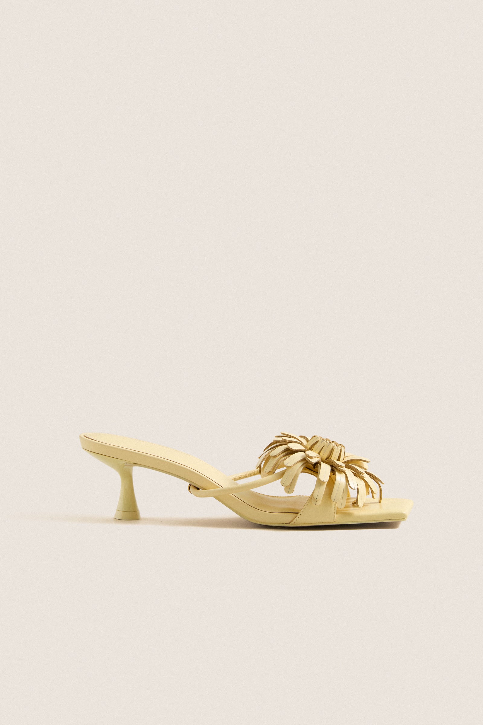 Buttercream Alora Low Heel: A classic, effortless sandal with a sculptural kitten heel, square toe, and removable floral motif, offering fun, high-end style.