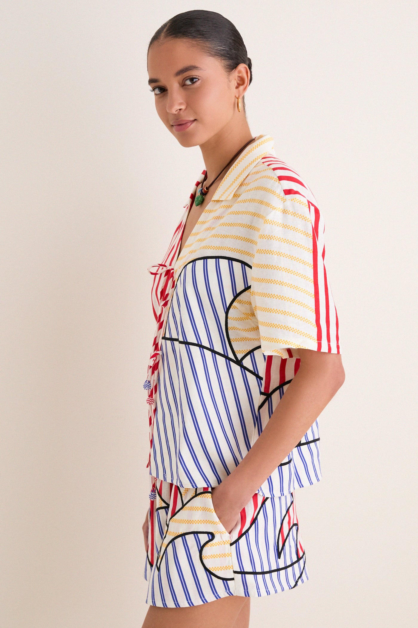 Young woman wearing the classic, effortless Navy Stripes Off-White Tie Front Blouse, featuring fun multi-colored stripes and high-end details, exuding a relaxed, playful charm.