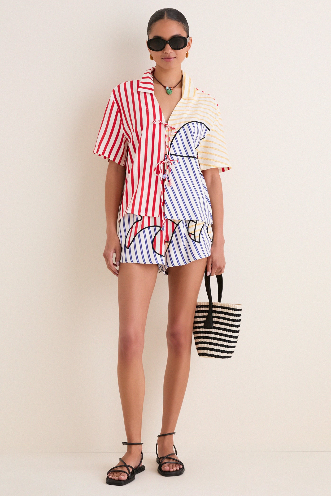 Model in the Navy Stripes Off-White Tie Front Blouse with matching shorts, exuding an effortless, fun vibe. A classic, high-end summer look completed with black sandals and a woven tote.