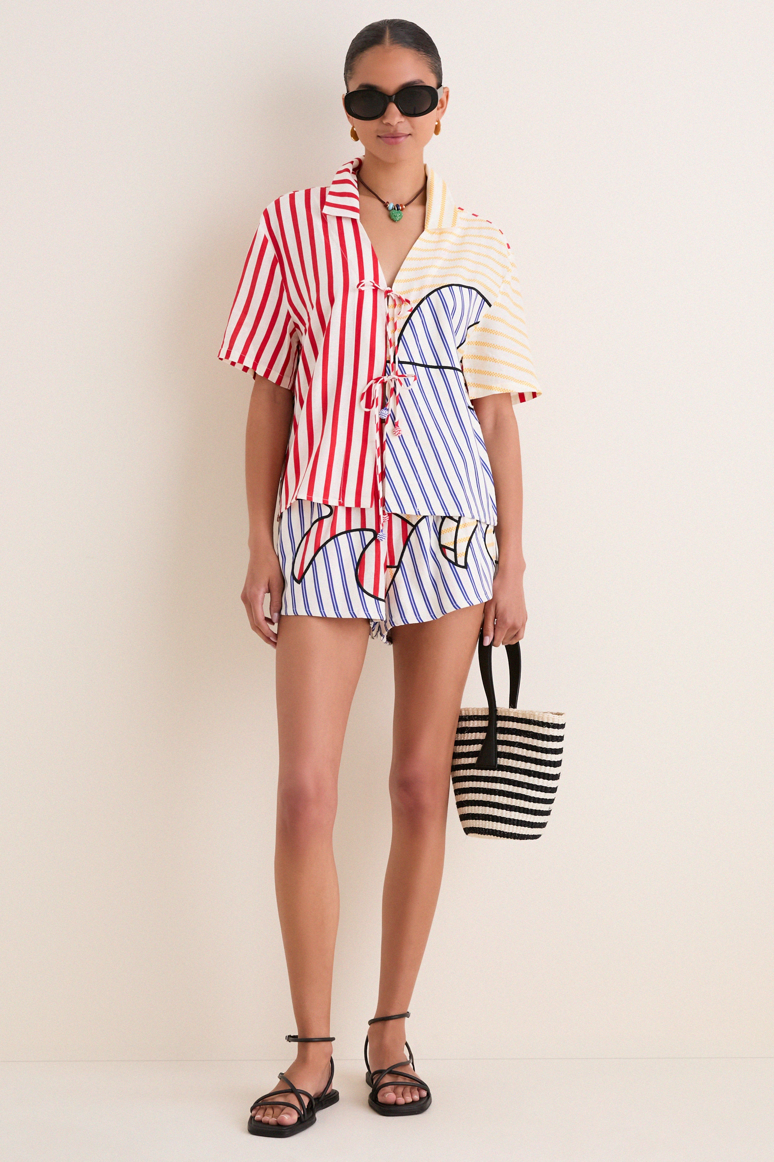 Model in the Navy Stripes Off-White Tie Front Blouse with matching shorts, exuding an effortless, fun vibe. A classic, high-end summer look completed with black sandals and a woven tote.