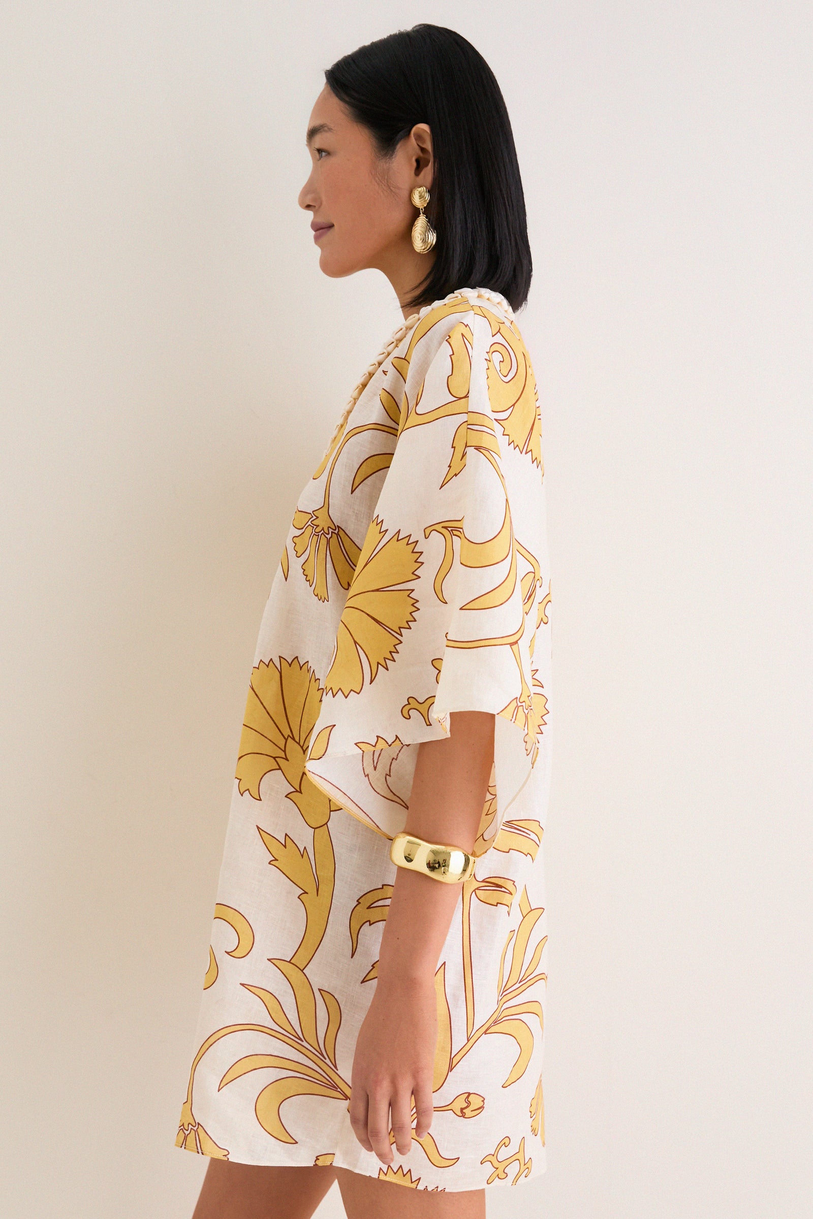 Woman in profile wearing Yellow Flowers Andina Hand-Embroidered Linen Mini Tunic with a relaxed fit and V-neckline, accessorized with gold jewelry, embodying classic, effortless style.
