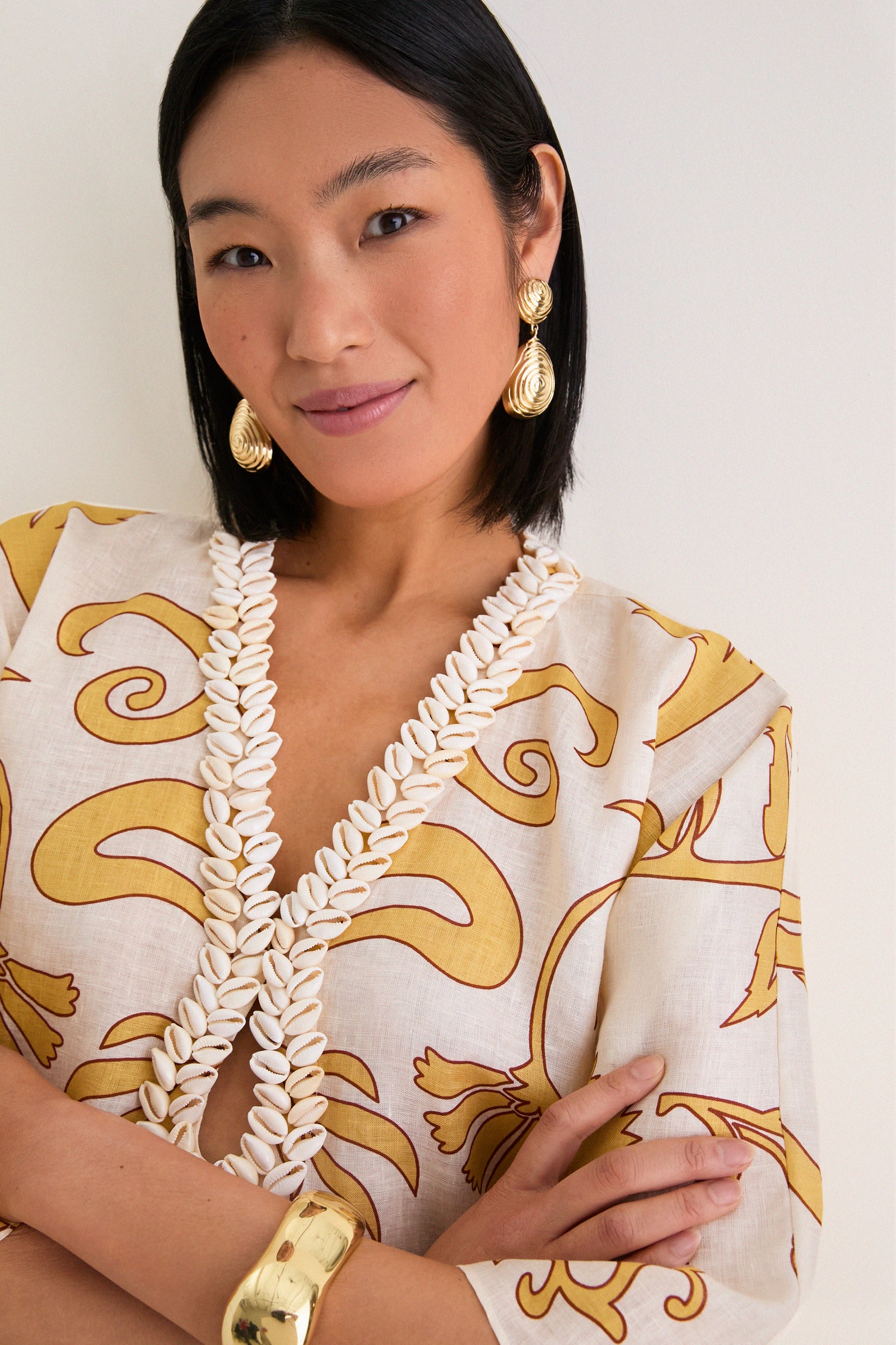 Woman in classic Yellow Flowers Andina Hand-Embroidered Linen Mini Tunic, featuring a V-neckline, wide sleeves, and bold gold accessories, embodying effortless, high-end style.