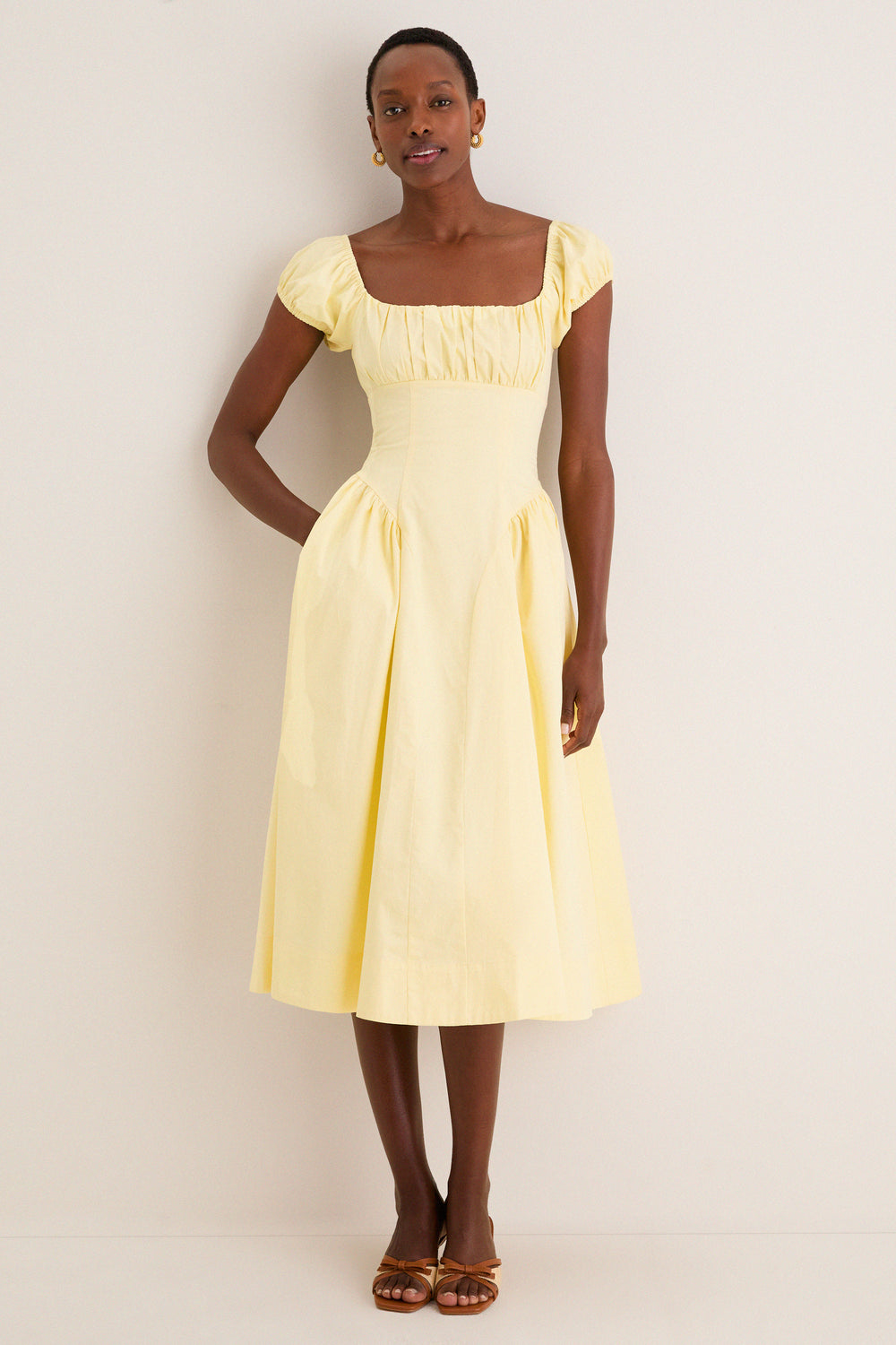 Woman models the classic Yellow Adilene Midi Dress with square neckline, fitted waist, and side seam pockets, styled effortlessly with sandals for a fun, high-end look.