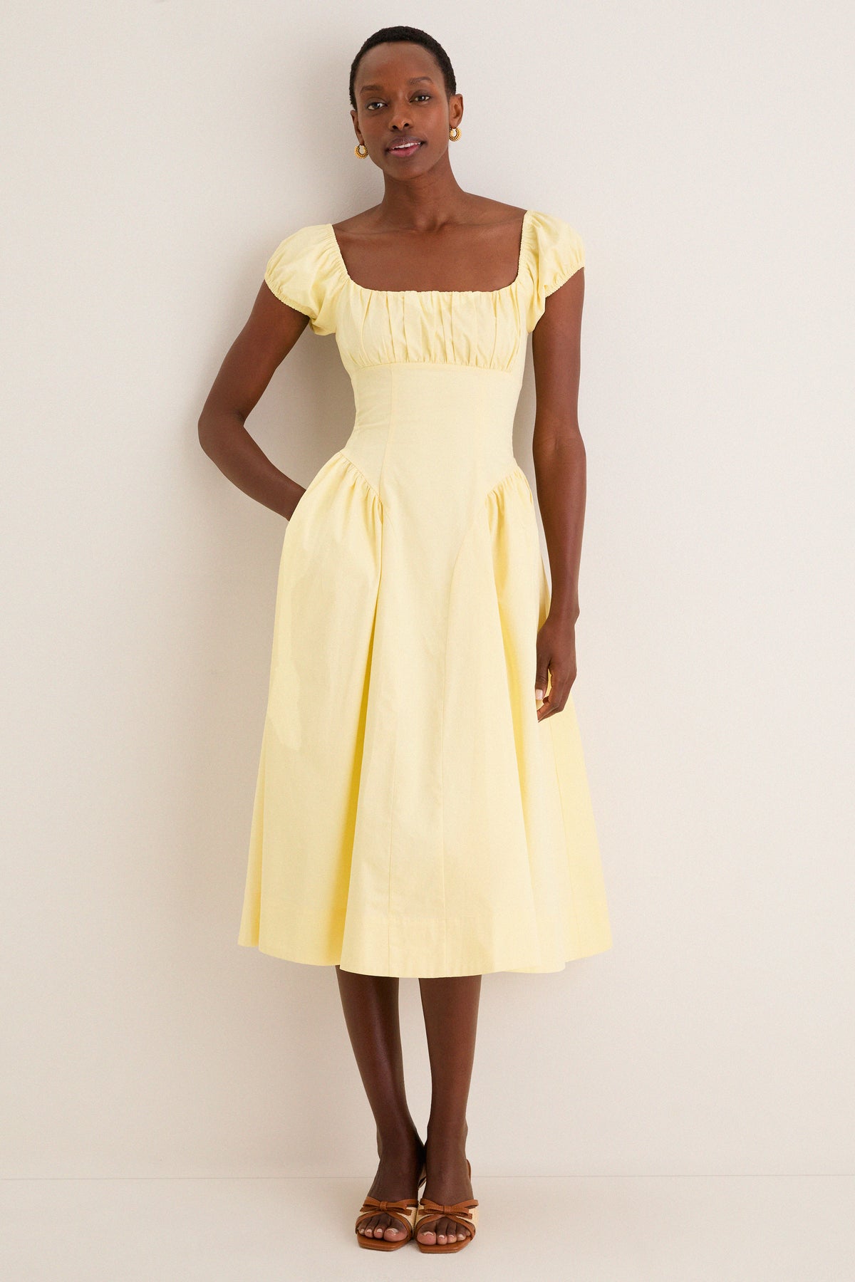 Woman models the classic Yellow Adilene Midi Dress with square neckline, fitted waist, and side seam pockets, styled effortlessly with sandals for a fun, high-end look.