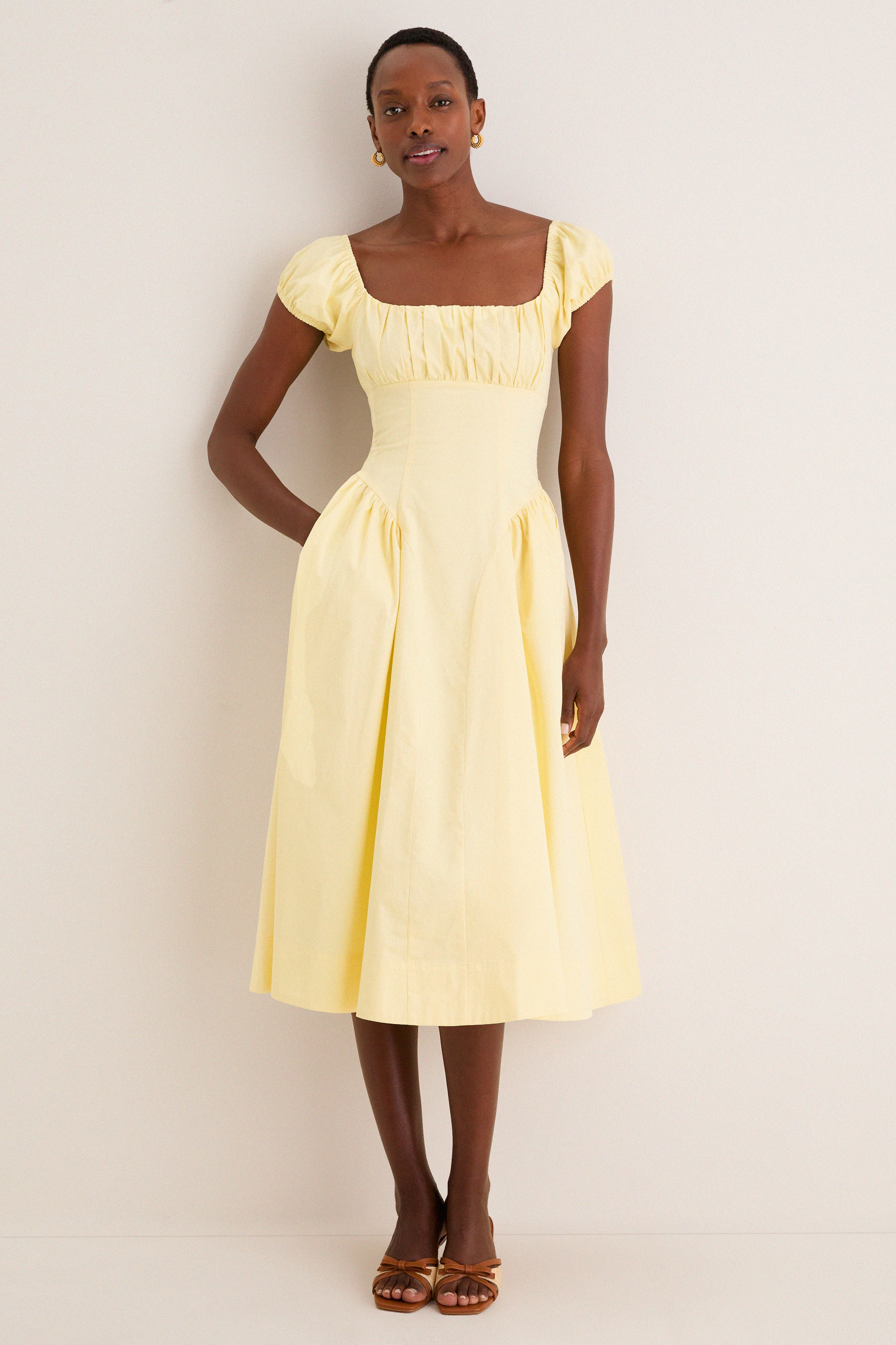 Woman models the classic Yellow Adilene Midi Dress with square neckline, fitted waist, and side seam pockets, styled effortlessly with sandals for a fun, high-end look.