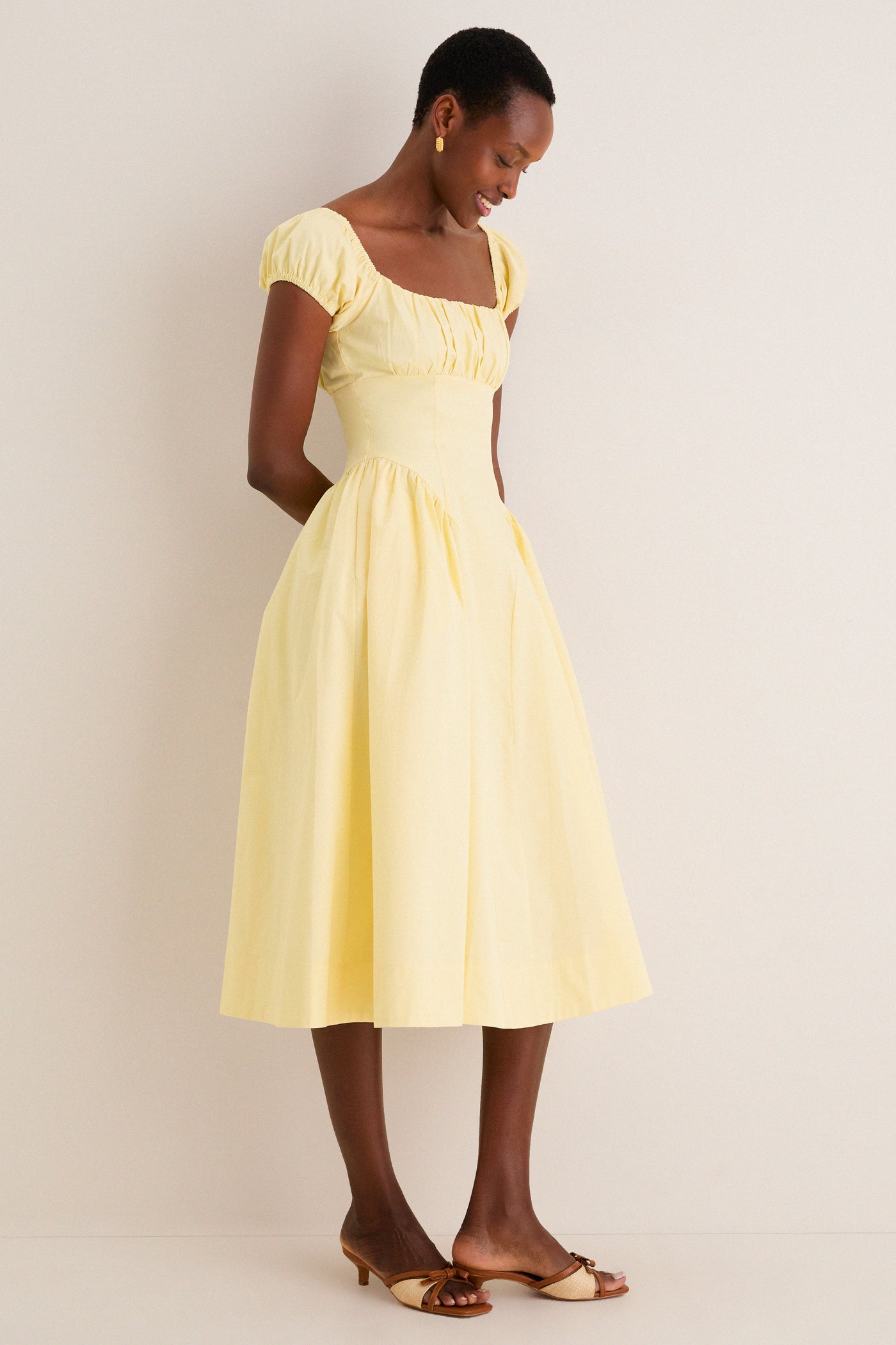 Woman in Yellow Adilene Midi Dress, featuring a classic fit-and-flare silhouette with puffed sleeves and side pockets, embodying an effortless, high-end style.
