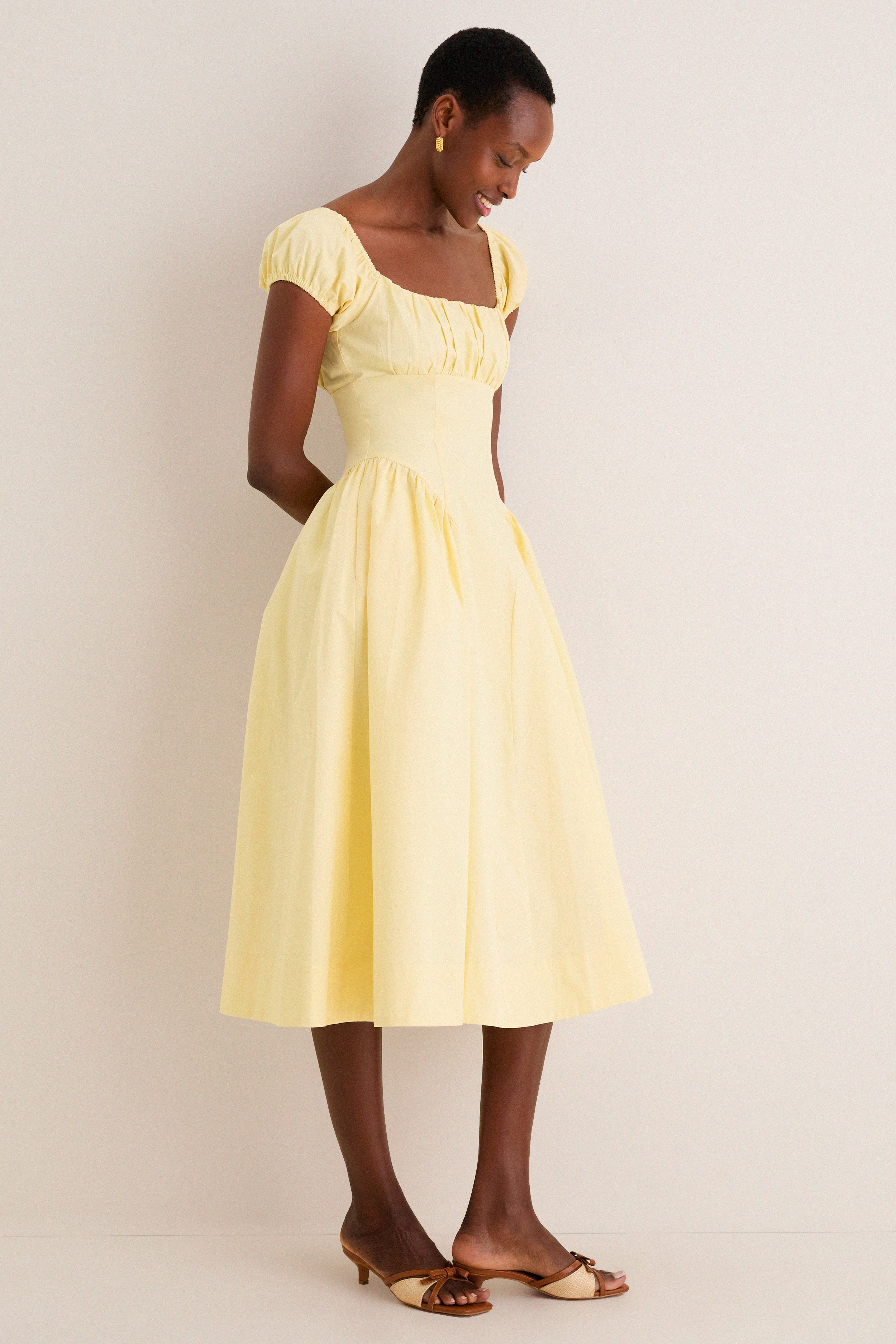 Woman in Yellow Adilene Midi Dress, featuring a classic fit-and-flare silhouette with puffed sleeves and side pockets, embodying an effortless, high-end style.