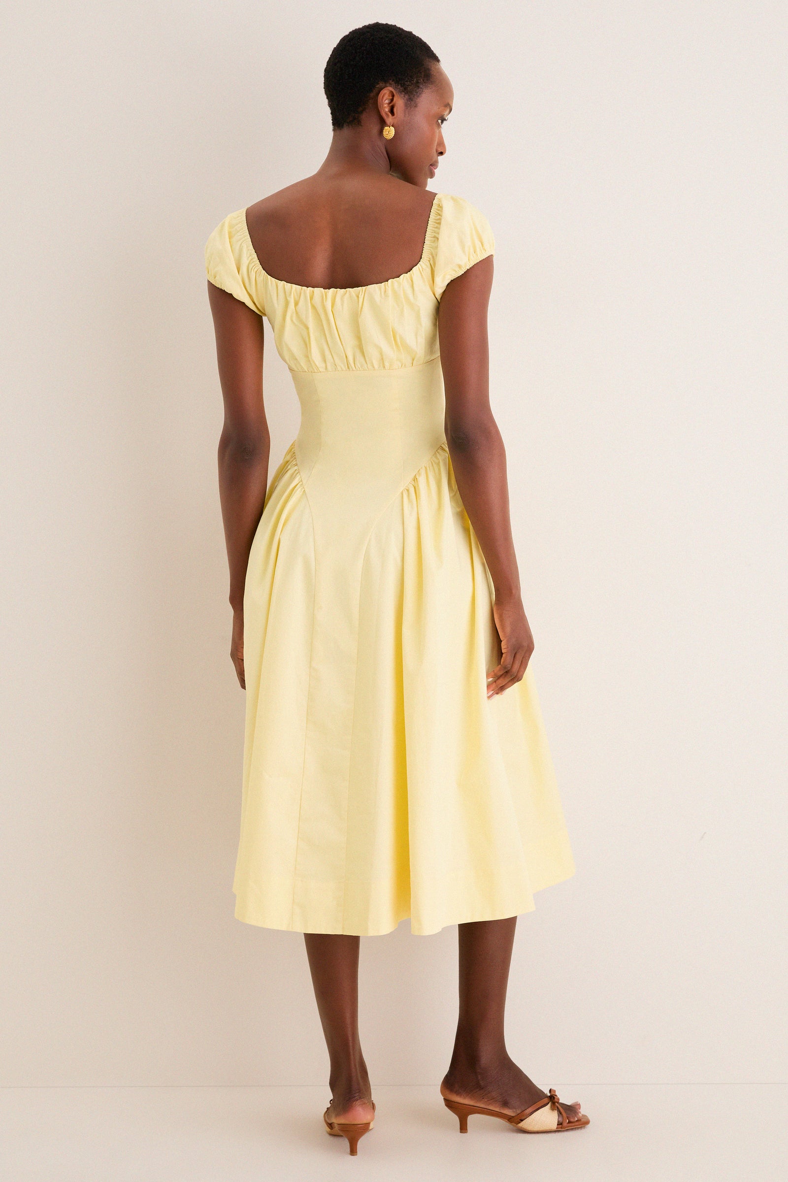 Woman wearing Yellow Adilene Midi Dress with puffed sleeves and flare skirt, embodying classic, effortless style. Perfect for fun, high-end occasions, paired with open-toe sandals.
