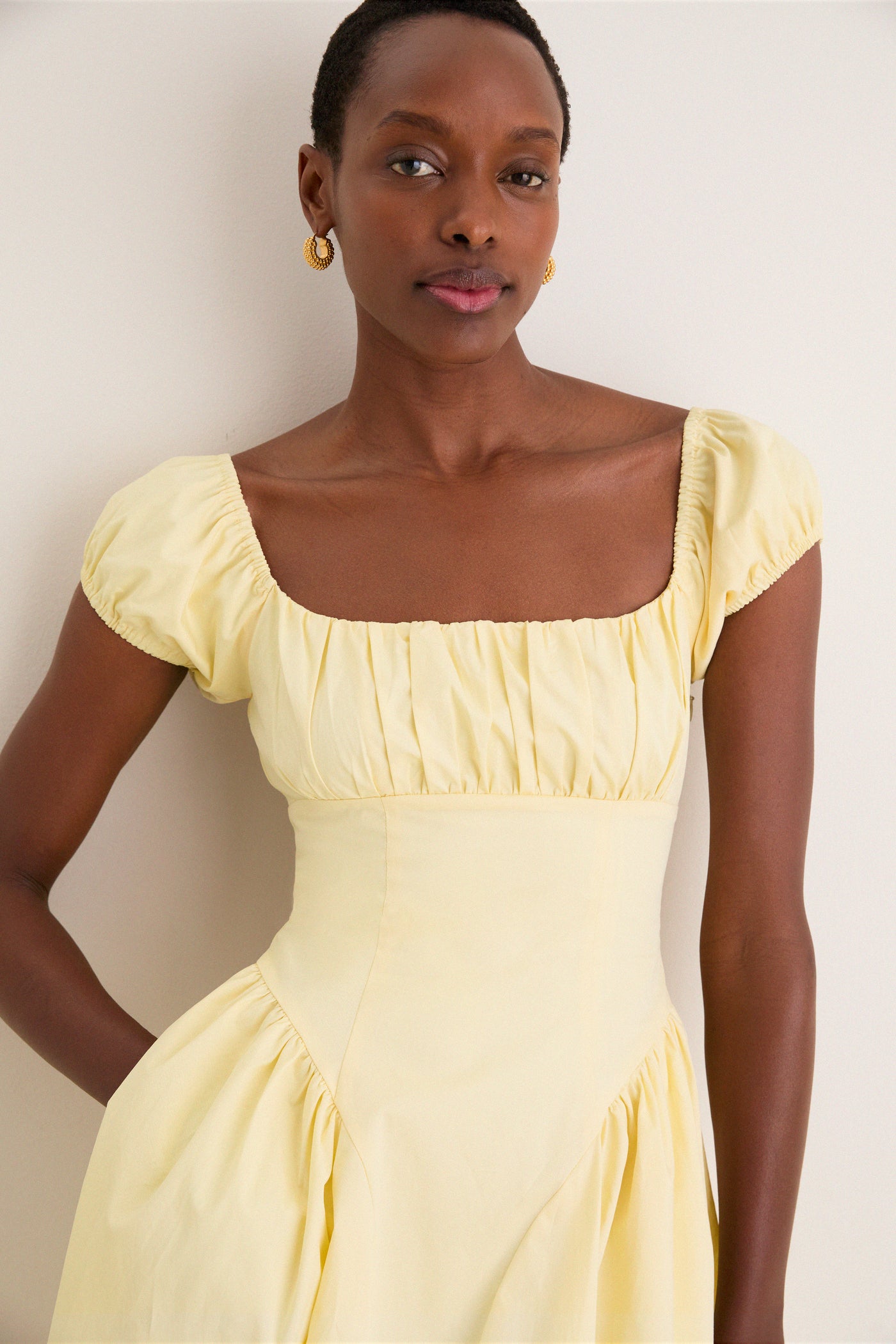 Woman wearing the classic Yellow Adilene Midi Dress, featuring a square neck, puff sleeves, and gold hoop earrings, embodying an effortless and high-end style.