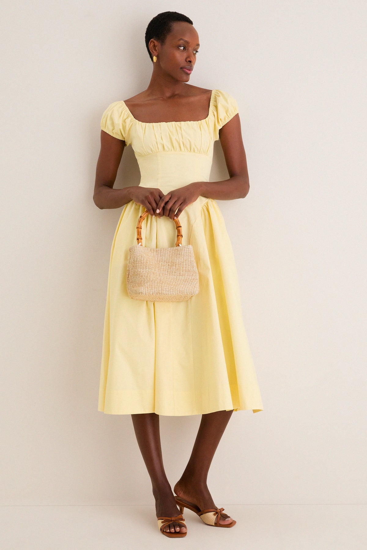 Yellow Adilene Midi Dress exudes effortless chic with its fitted waist, puff sleeves, and classic square neck, paired with a woven handbag and heeled sandals for a high-end, fun look.