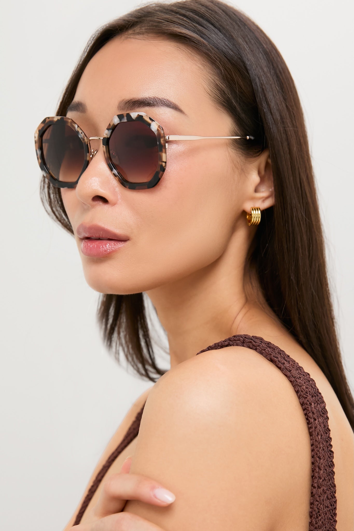 Woman in profile wearing Brown Tortoise Angie Sunglasses; oversized, hexagonal tortoiseshell frames with gold temples, embodying classic, effortless, and fun high-end style.