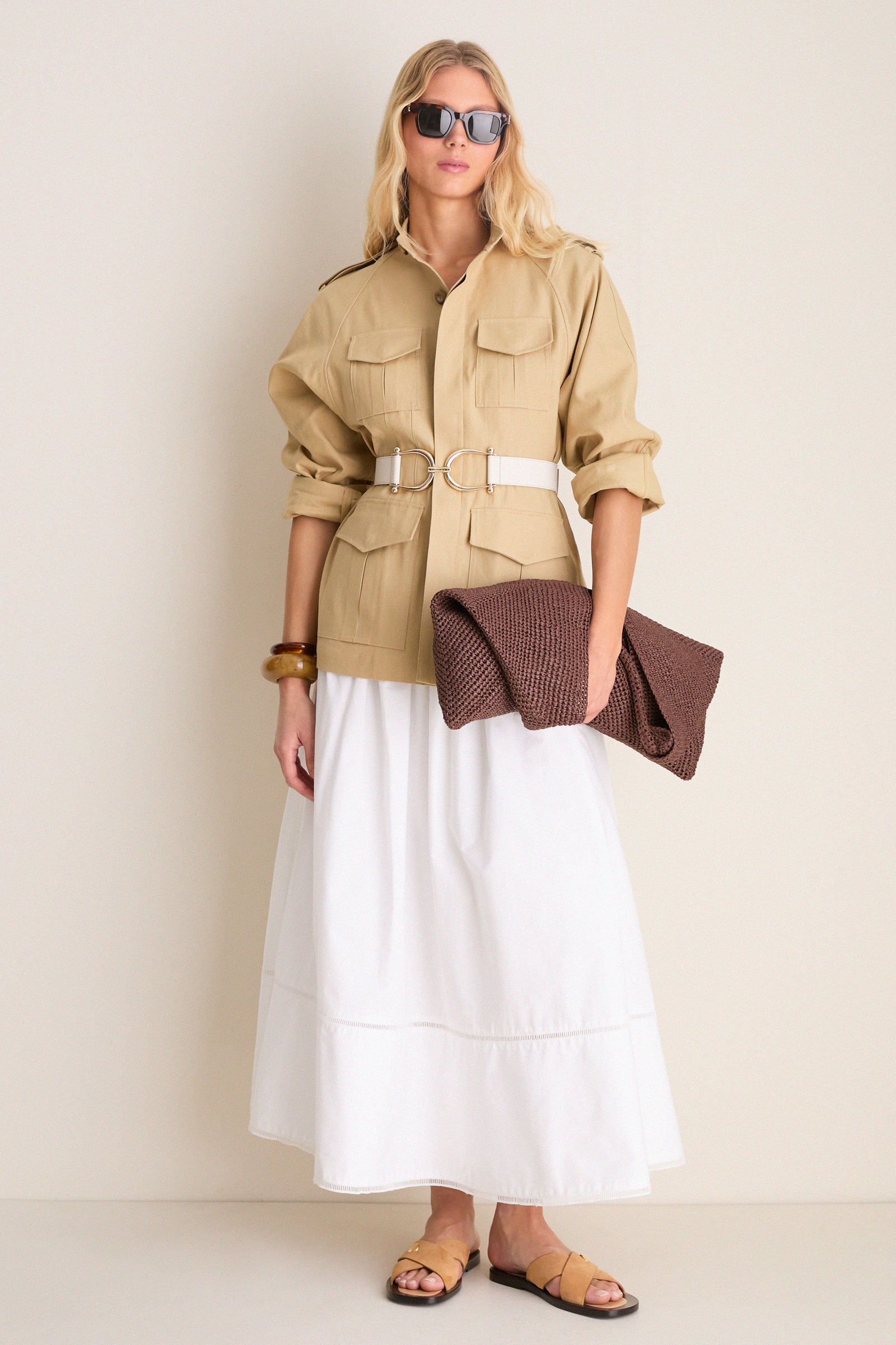 Woman models a classic, high-end look featuring the Gesso Grant Belt with equestrian-style buckles, effortlessly cinching a safari-style jacket over a flowing skirt.