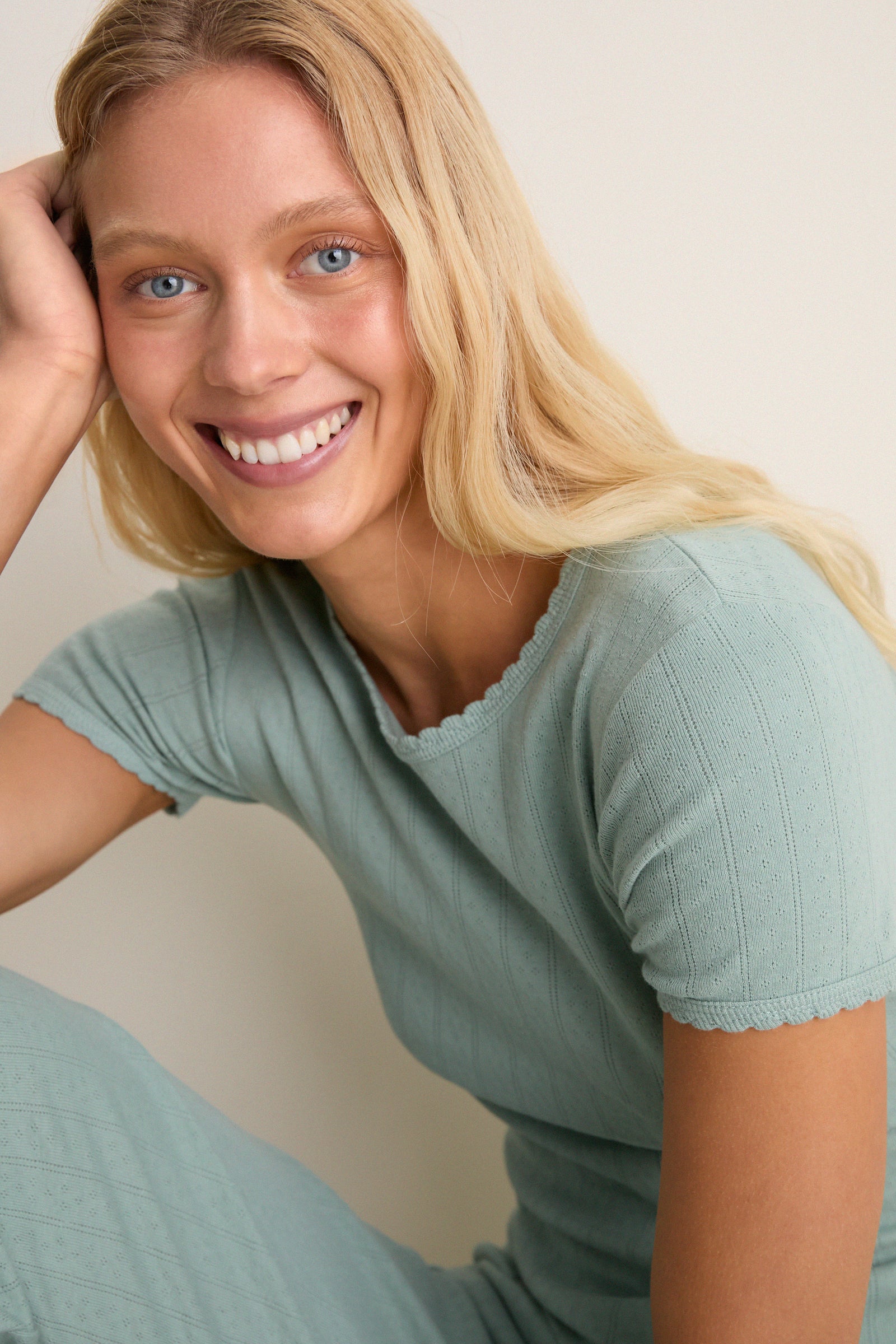 Young woman smiling in Eucalyptus Slim Fit Pointelle Tee, showcasing classic, effortless style with scalloped edges and eyelet details, embodying high-end, fun elegance.