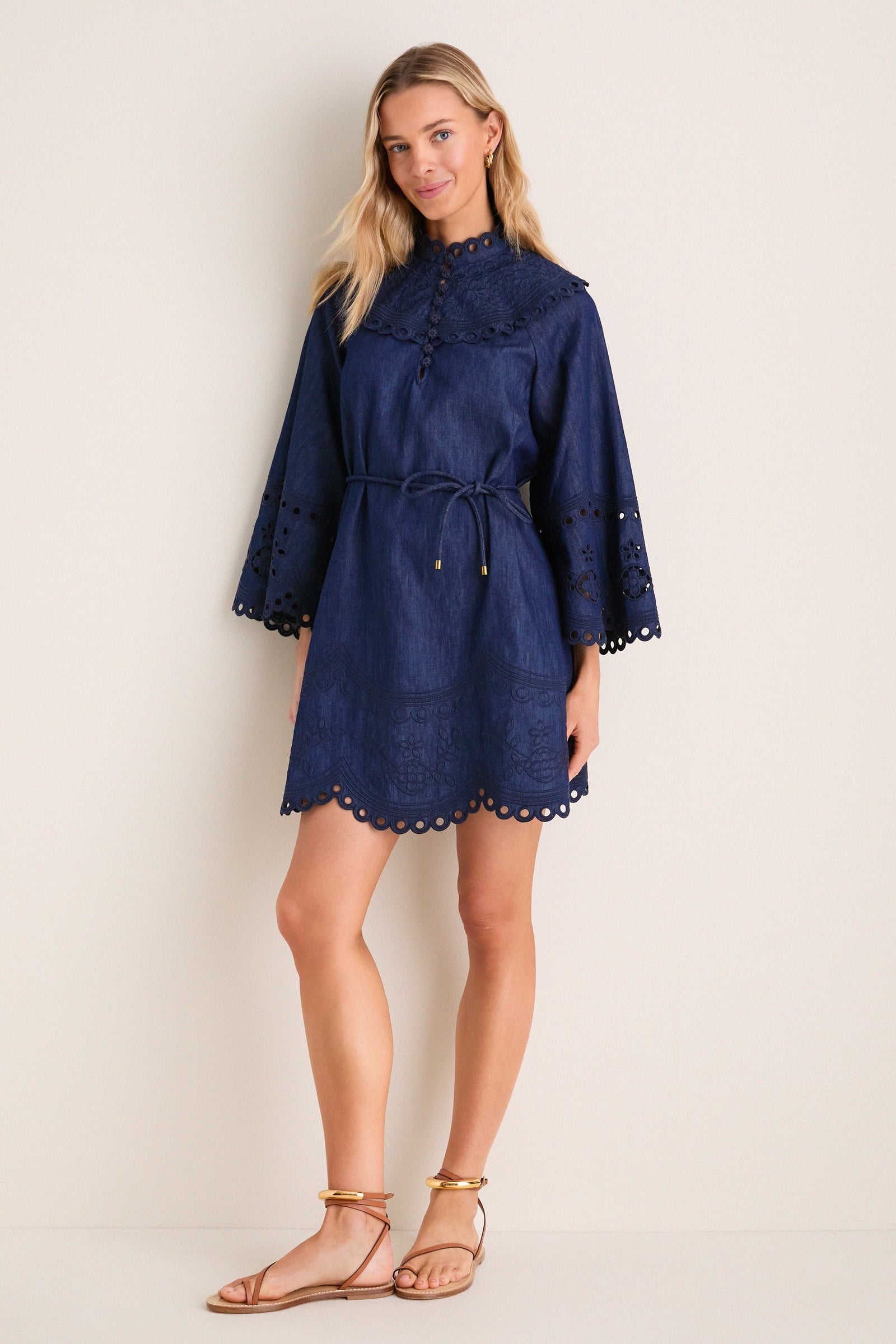 Model in Ink Mahon Broderie Denim Mini Dress with scalloped collar and bell sleeves, embodying classic elegance. Styled with flat sandals for an effortless, high-end daytime look.