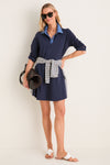 Woman models the classic Denim Collar Carolyn Swing Mini Dress, paired with a fun striped sweater, high-end scalloped sandals, and an effortless woven tote, exuding confidence.