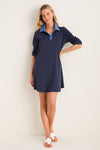 Young woman in the Denim Collar Carolyn Swing Mini Dress, showcasing its classic navy style with an effortless, fun vibe, paired with high-end white scallop-edged thong sandals.