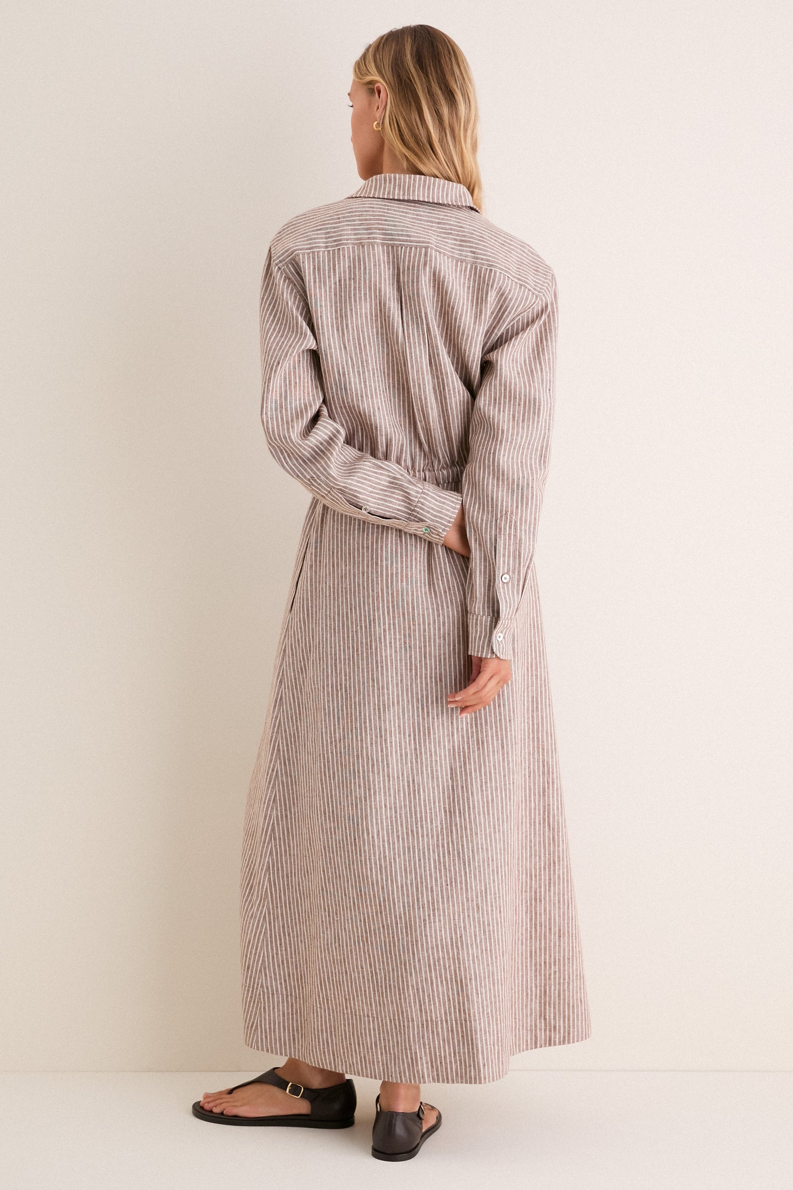 Woman wearing the classic Cafe Stripe Linen Julien Shirt Dress with a cinched waist and buttoned cuffs, paired effortlessly with black leather sandals for a high-end, fun look.