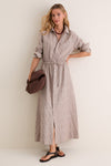 Woman models the classic Cafe Stripe Linen Julien Shirt Dress, featuring an effortless collared neckline, rolled sleeves, and drawstring waist, paired with a chunky-knit sweater and accessories.