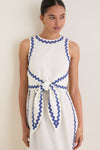 Young woman wearing the classic White Ric Rac Tie-Front Brocks Dress, featuring effortless periwinkle-blue trim and a fun, high-end bow detail at the waist.