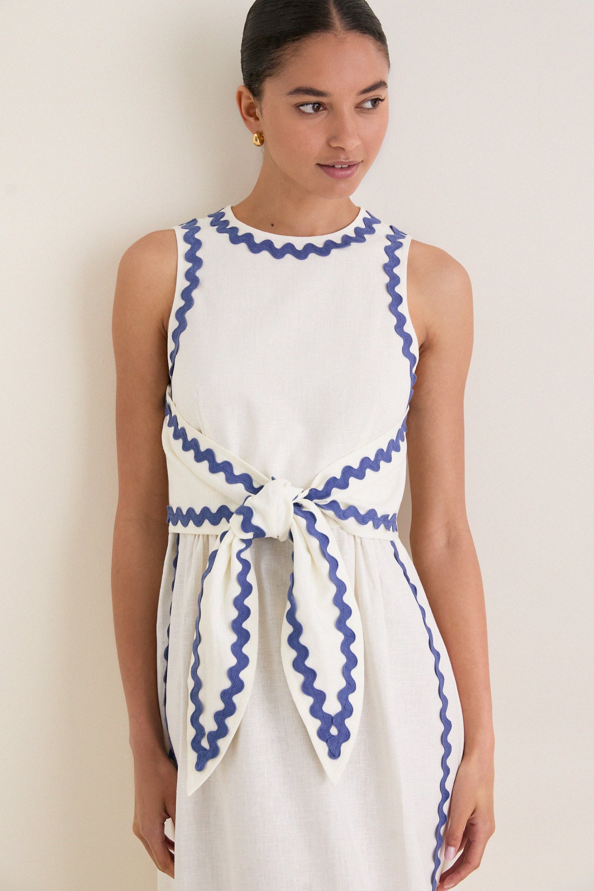Young woman wearing the classic White Ric Rac Tie-Front Brocks Dress, featuring effortless periwinkle-blue trim and a fun, high-end bow detail at the waist.