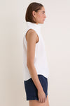Woman models the classic White Sleeveless Bessette Button Down with stand collar and hidden buttons, paired with navy shorts for an effortless, high-end summer look.