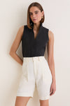 Model wearing the Black Sleeveless Bessette Button Down, a classic, high-end top with a stand collar, styled effortlessly with tailored white shorts for a fun, chic look.