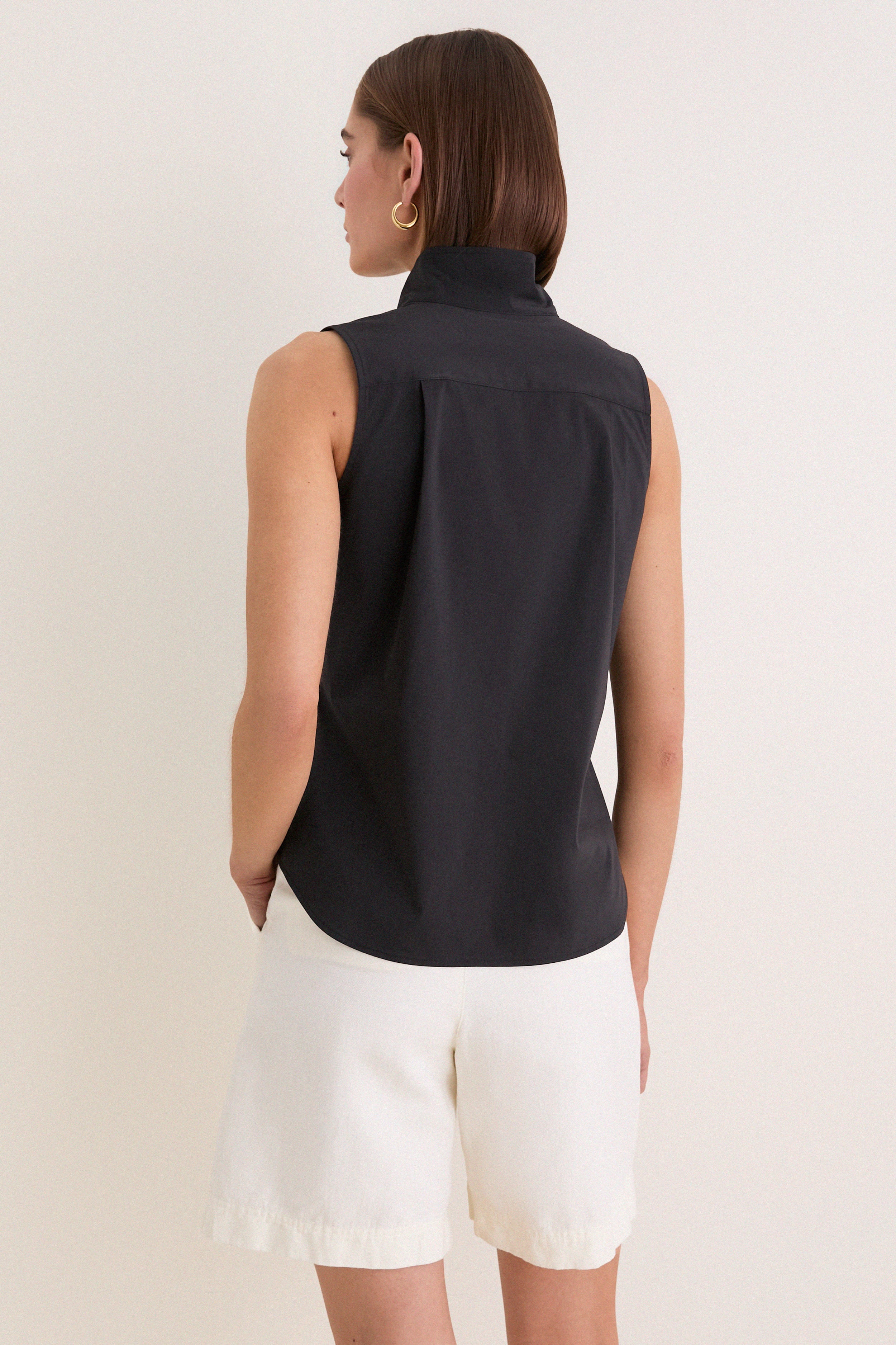 Woman in Black Sleeveless Bessette Button Down, showcasing a classic, effortless, high-end style with a stand collar and hidden button placket for a fun summer look.