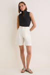 Woman in a classic, high-end Black Sleeveless Bessette Button Down, styled with white shorts and snakeskin-print sandals, exudes effortless and fun sophistication.