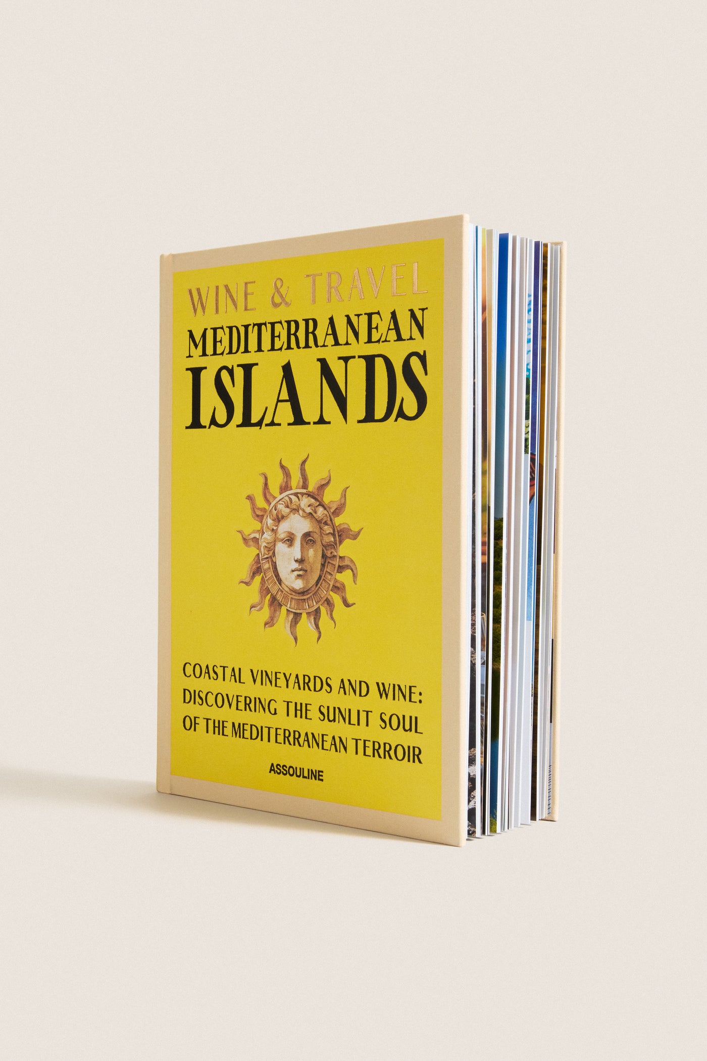 Hardcover book titled Wine & Travel Mediterranean Islands by Assouline, featuring a classic sun-face motif, promises an effortless, fun journey through high-end Mediterranean wine culture.